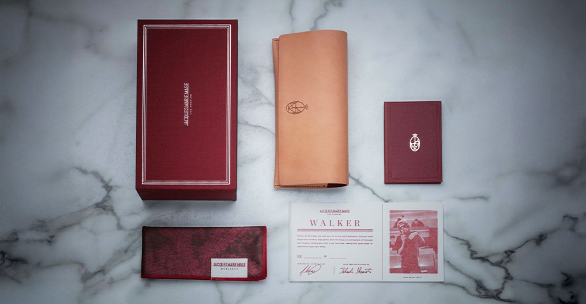 Jacques Marie Mage Walker sunglasses gift set, top view: marble base, red box, tan leather case, booklet, certificate, wallet, photo card.