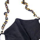 A black fabric face mask with the Small Link Necklace Chain for Face Masks, featuring a gold and black tortoiseshell pattern, used as a strap and displayed against a white background.