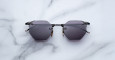 The Jacques Marie Mage El Dorado sunglasses, featuring geometric hexagonal black frames and dark lenses, are displayed on a white marble surface.
