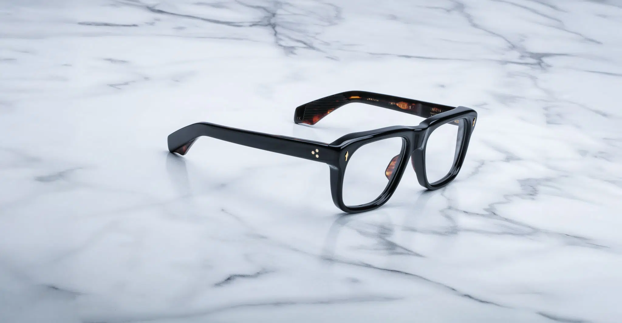 Jacques Marie Mage Yves black-framed sunglasses with blue lenses are displayed on a white marble surface with grey veining.