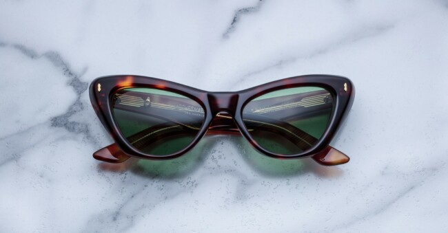 A pair of cat-eye sunglasses with dark green lenses and a brown tortoiseshell frame rests on a light gray marble surface.