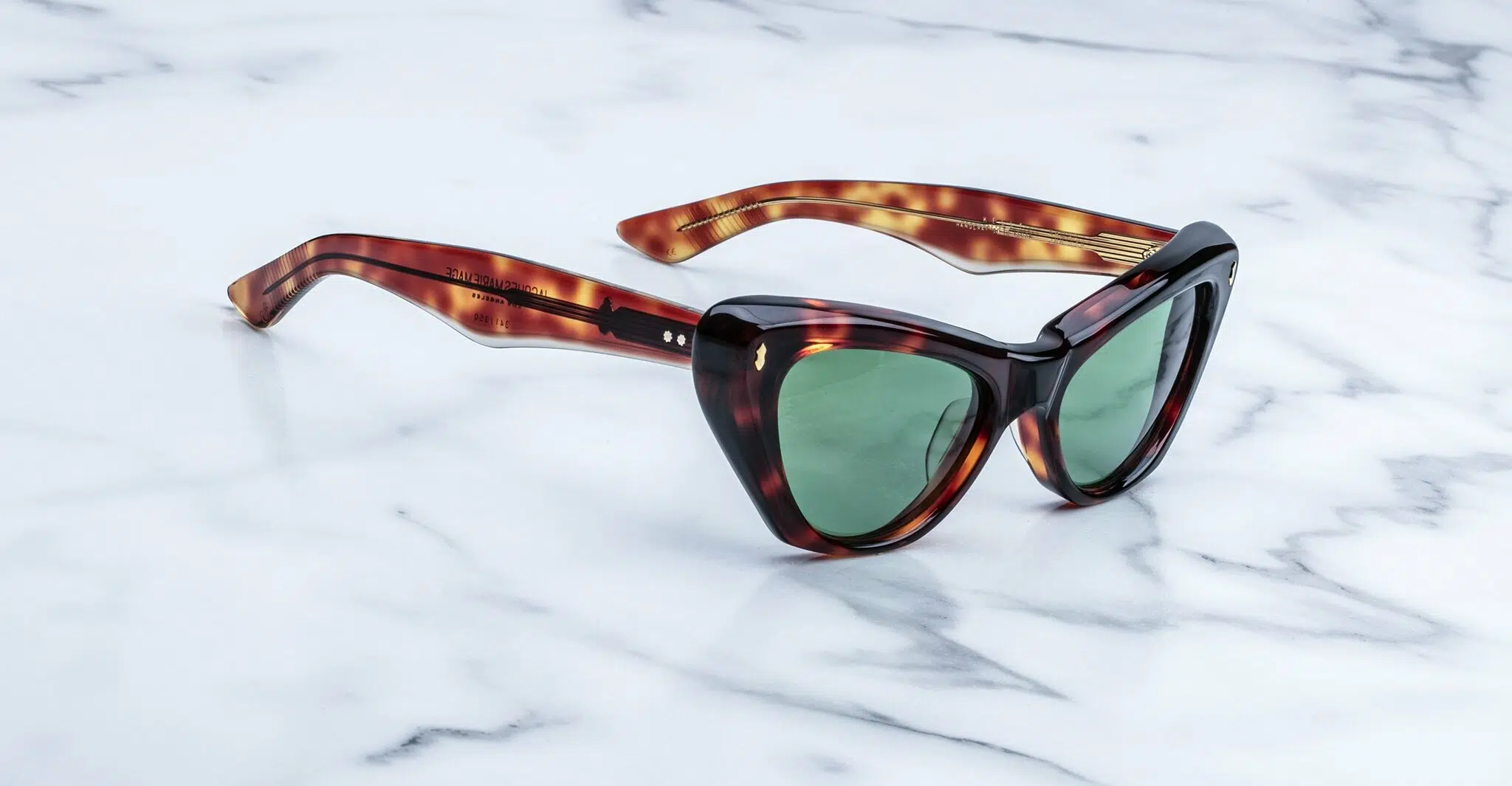 A pair of tortoiseshell cat-eye sunglasses with green lenses is placed on a white marble surface.