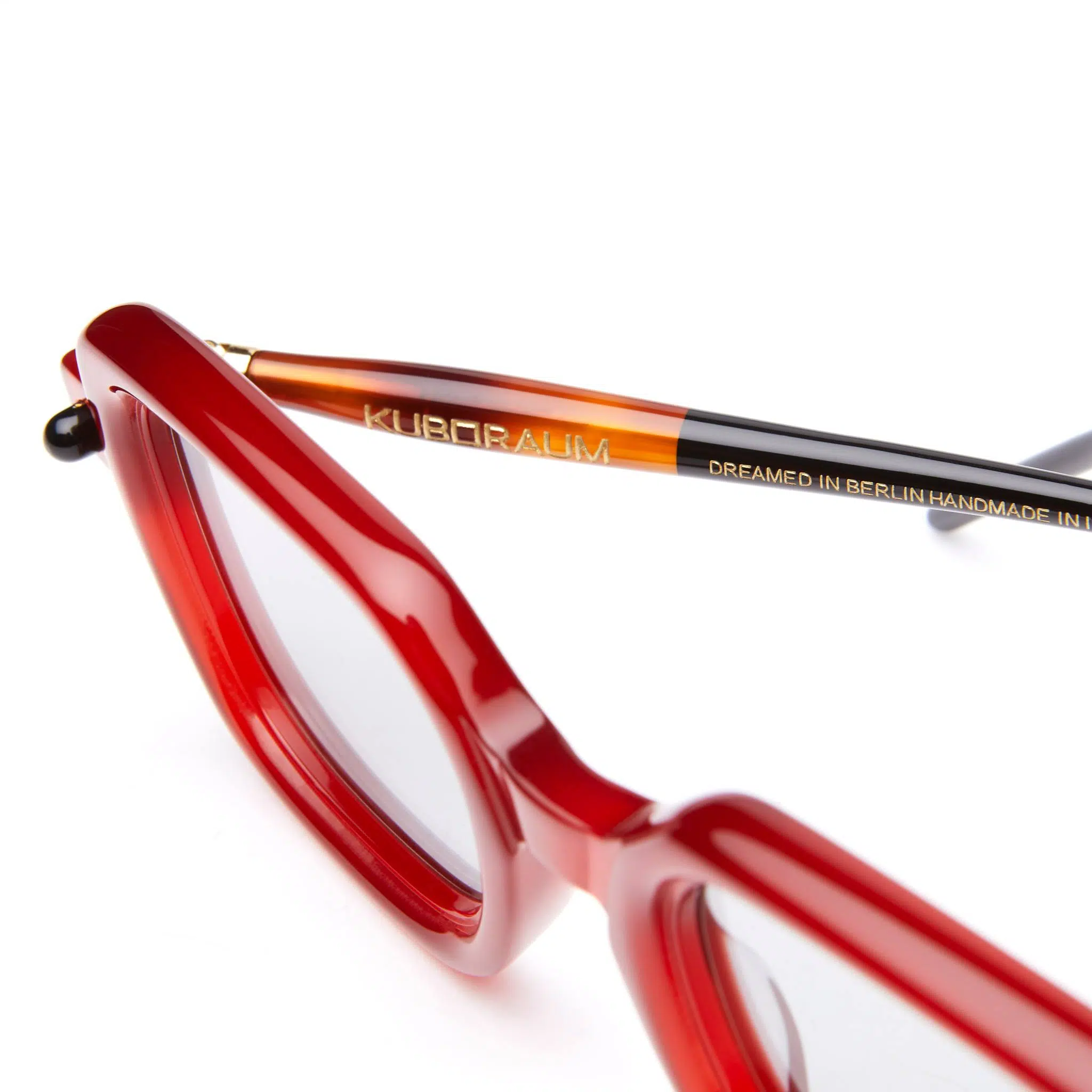 Close-up of red eyeglass frames with focus on the arm, which has the brand name Kuboraum and the text Dreamed in Berlin Handmade in... printed in gold.