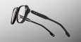 The Jacques Marie Mage Shozo eyeglasses feature black thick-rimmed frames with clear lenses, viewed from an angled side perspective on a light gray background. Two small white star accents adorn the temples.