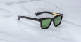 A pair of Jacques Marie Mage Lankaster black sunglasses with green lenses and gold temple accents, displayed on a white marble surface.