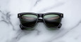 A pair of Jacques Marie Mage Lankaster black rectangular sunglasses with dark green lenses rests on a white marble surface.