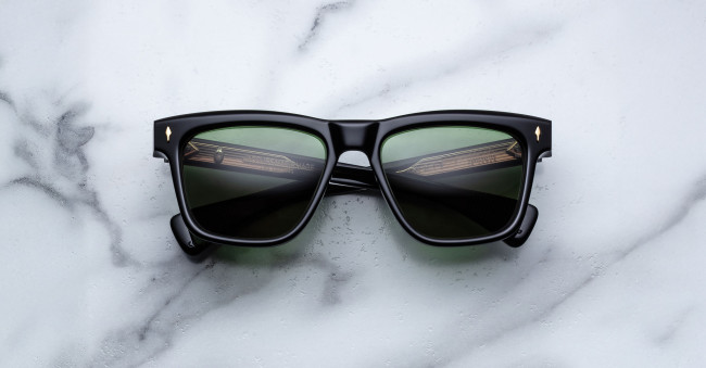A pair of Jacques Marie Mage Lankaster black rectangular sunglasses with dark green lenses rests on a white marble surface.