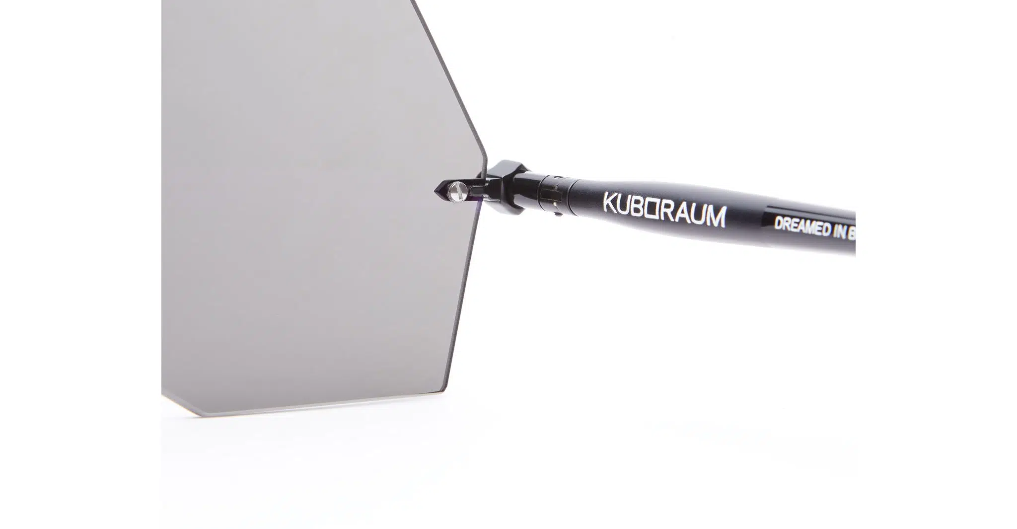 Close-up of a hexagonal lens from the Kuboraum P90 sunglasses with a black arm and white KUBORAUM DREAMED IN BERLIN text, set against a plain white background.