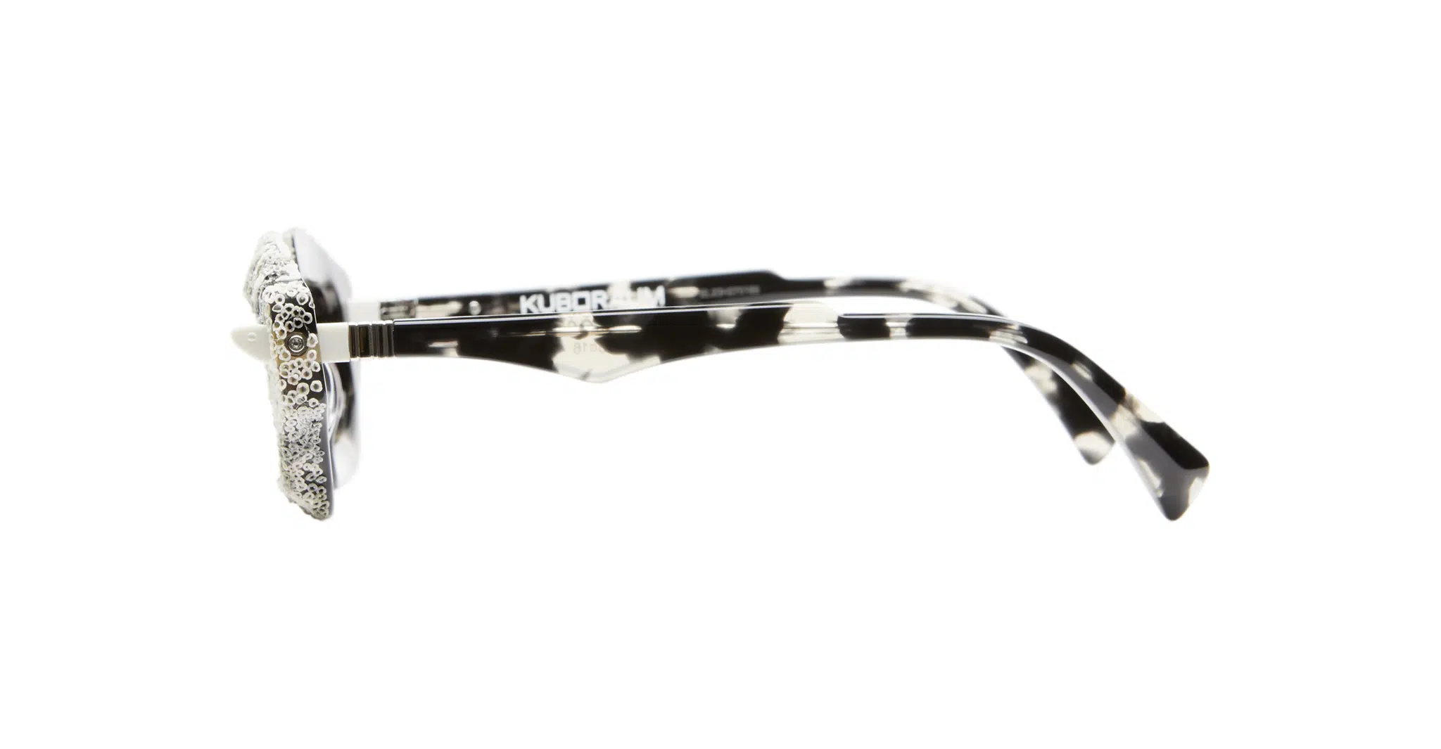 Kuboraum-Q6-HG-WC-White-Coral-KRS0Q6HG00WC252Y-Side-Dan-Deutsch Side view of Kuboraum Q6 eyeglasses featuring black and white marbled frames with decorative rhinestones on the lens edges, displayed against a plain white background.