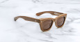 The Jacques Marie Mage Dealan X Umit Benan are brown rectangular sunglasses with thick frames and dark lenses, shown on a white marble surface. The temples have small decorative details near the hinges.