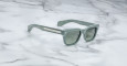 The Jacques Marie Mage Molino sunglasses, featuring mint green square frames, dark lenses, and silver temple details, rest on a white marble surface.