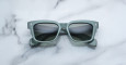 A pair of Jacques Marie Mage Molino sunglasses, featuring a square shape, matte green frames, and dark lenses, rests on a white marble surface.