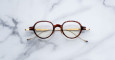 The Jacques Marie Mage Clark, round tortoiseshell eyeglasses with gold temples, are displayed from above on a white marble surface.