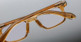 Close-up of Jacques Marie Mage Moscova eyeglasses, featuring translucent amber frames and clear lenses, with detailed texture and reflections on the frame set against a neutral gray background.