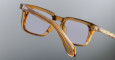A close-up view of the side and front of the Jacques Marie Mage Moscova square translucent brown eyeglasses with clear lenses, displayed against a plain gray background.