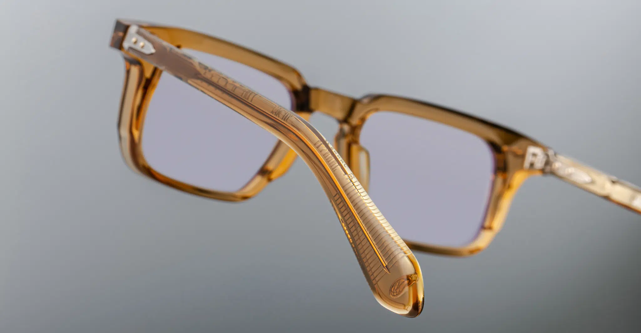 A close-up view of the side and front of the Jacques Marie Mage Moscova square translucent brown eyeglasses with clear lenses, displayed against a plain gray background.