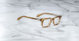 The Jacques Marie Mage Moscova brown transparent square-frame eyeglasses are displayed on a white marble surface with gray veining.
