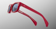 The Jacques Marie Mage Initials red acetate sunglasses feature thick frames, dark lenses, and white printed branding on the inside arm. Shown from a side angle against a light gray gradient background.