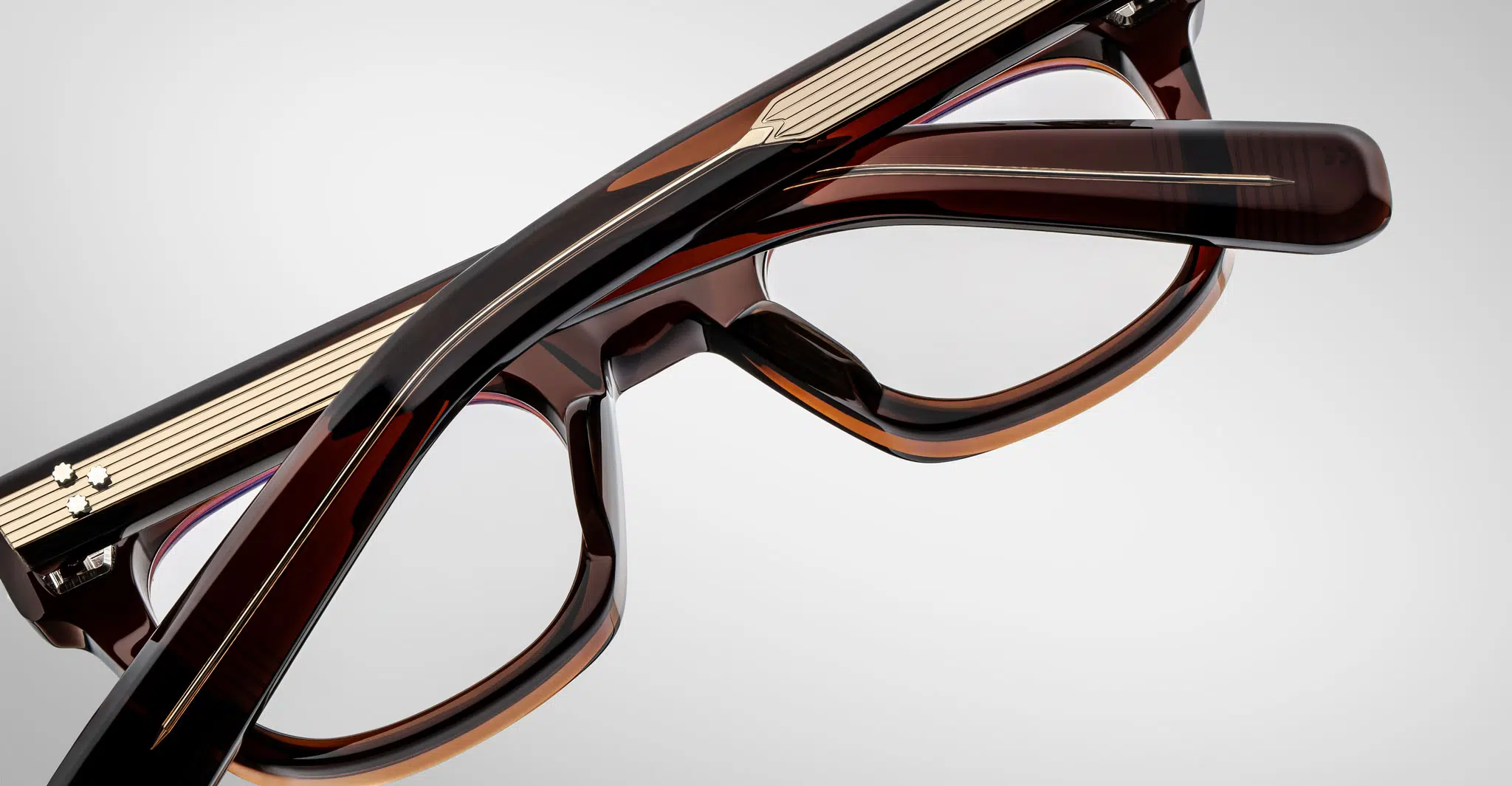 Close-up of Jacques Marie Mage Godard glasses with thick, glossy brown frames and subtle striped details, showing the temples, bridge, and part of the lenses against a plain background.