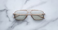 The Jacques Marie Mage Earl gold-framed rectangular eyeglasses with lightly tinted lenses rest on a white marble surface.