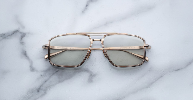 The Jacques Marie Mage Earl gold-framed rectangular eyeglasses with lightly tinted lenses rest on a white marble surface.