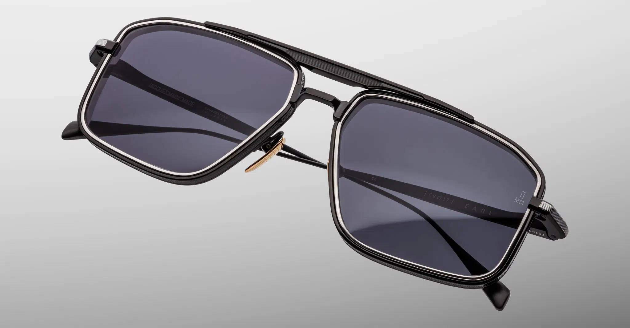 Jacques-Marie-Mage-Earl-Corbeau-JMMER-19J-Detail1-Dan-Deutsch The Jacques Marie Mage Earl sunglasses feature a rectangular black frame, dark tinted lenses, and a double bridge design, shown against a plain light gray background.