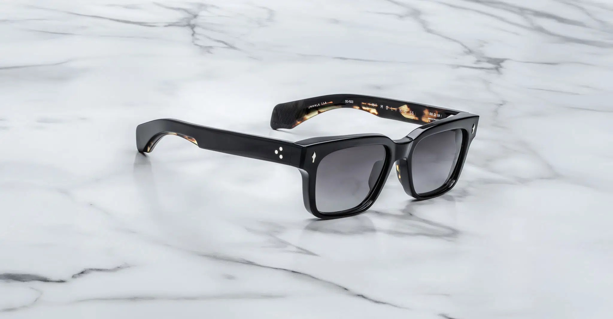The Jacques Marie Mage Molino 55 black rectangular sunglasses with dark lenses rest on a white marble surface with gray veining.