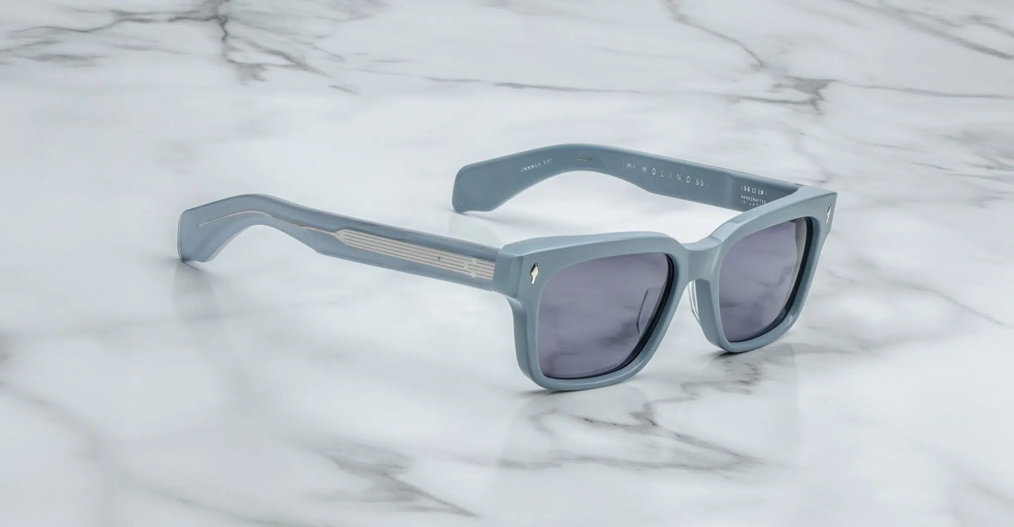 Jacques-Marie-Mage-Molino-55-Tiger-JMMMLX-10T-3-4-Dan-Deutsch The Jacques Marie Mage Molino 55: light blue square sunglasses with dark lenses and thick frames are displayed on a white marble surface.