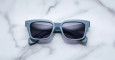 A pair of Jacques Marie Mage Molino 55 blue rectangular sunglasses with dark lenses rests on a white marble surface.