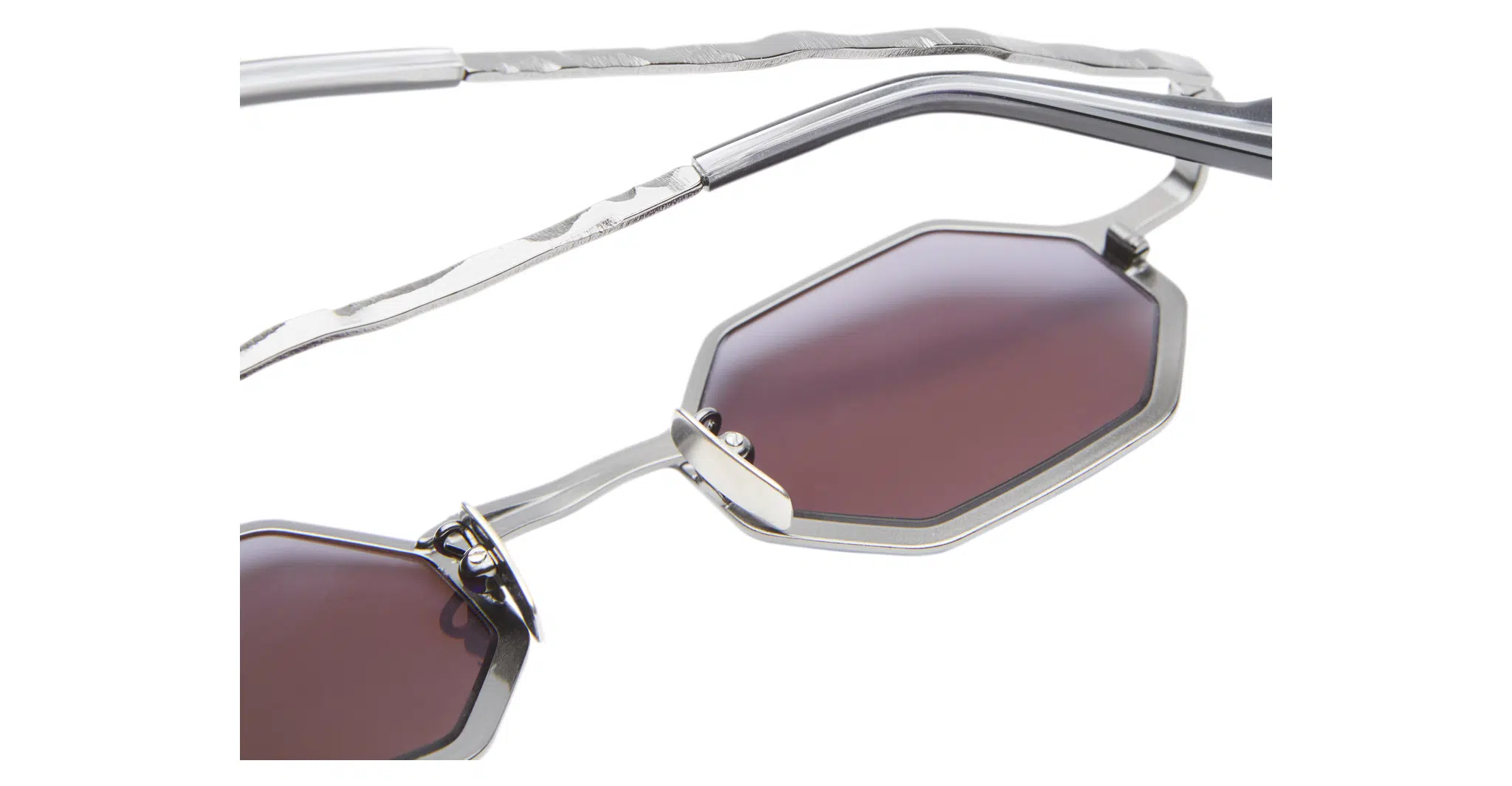 Kuboraum-Z19-GMG-Gun-Metal-KRSZ19GMG00000GF-Detail1-Dan-Deutsch Close-up of Kuboraum Z19 sunglasses with octagonal, burgundy-tinted lenses and thin silver metal frames featuring a wavy, textured temple design.