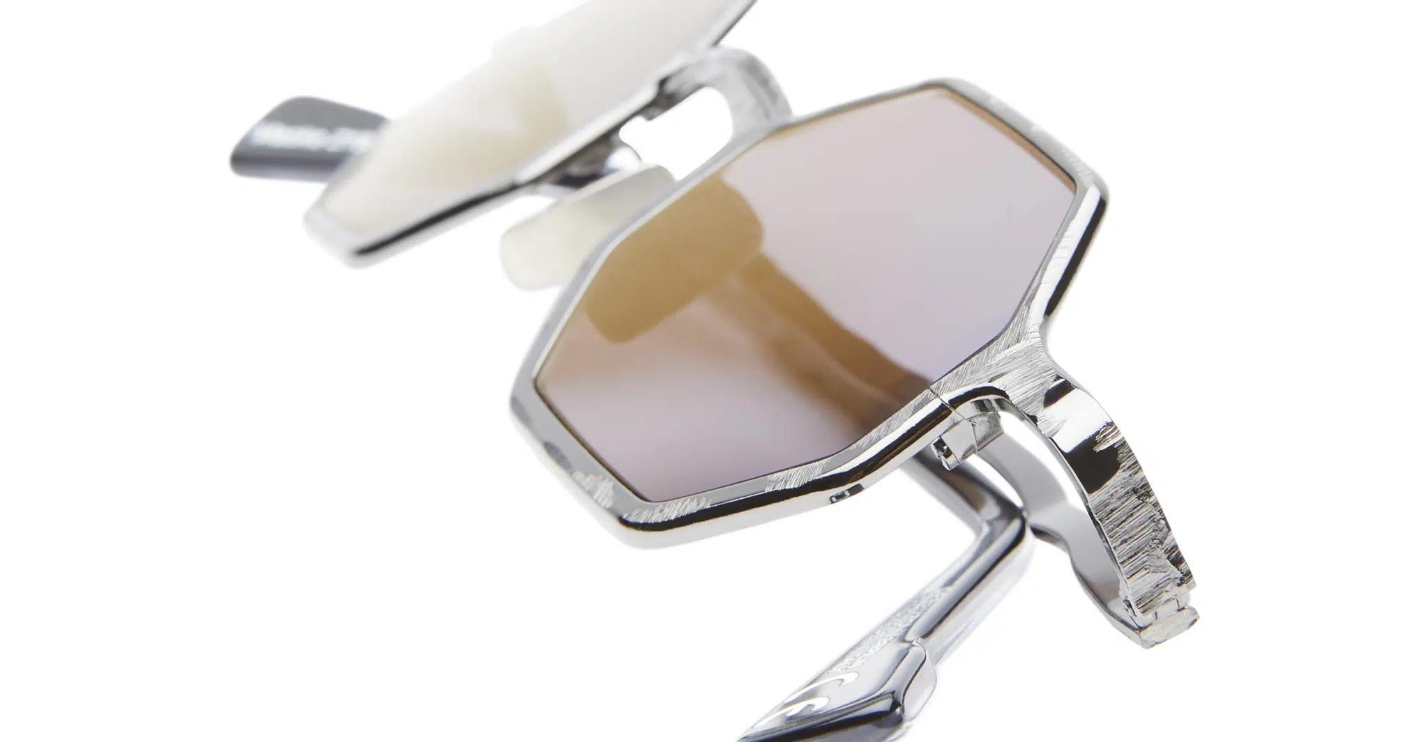 Kuboraum-Z19-GMG-Gun-Metal-KRSZ19GMG00000GF-Detail4-Dan-Deutsch Close-up of Kuboraum Z19 geometric sunglasses featuring brown-tinted lenses and sleek silver frames, shown partly folded against a white background.