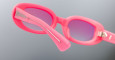 Close-up of Jacques Marie Mage Besset pink sunglasses with gradient purple lenses, highlighting the inside of the frame, arm, and visible metal hinge and bar against a plain gray background.