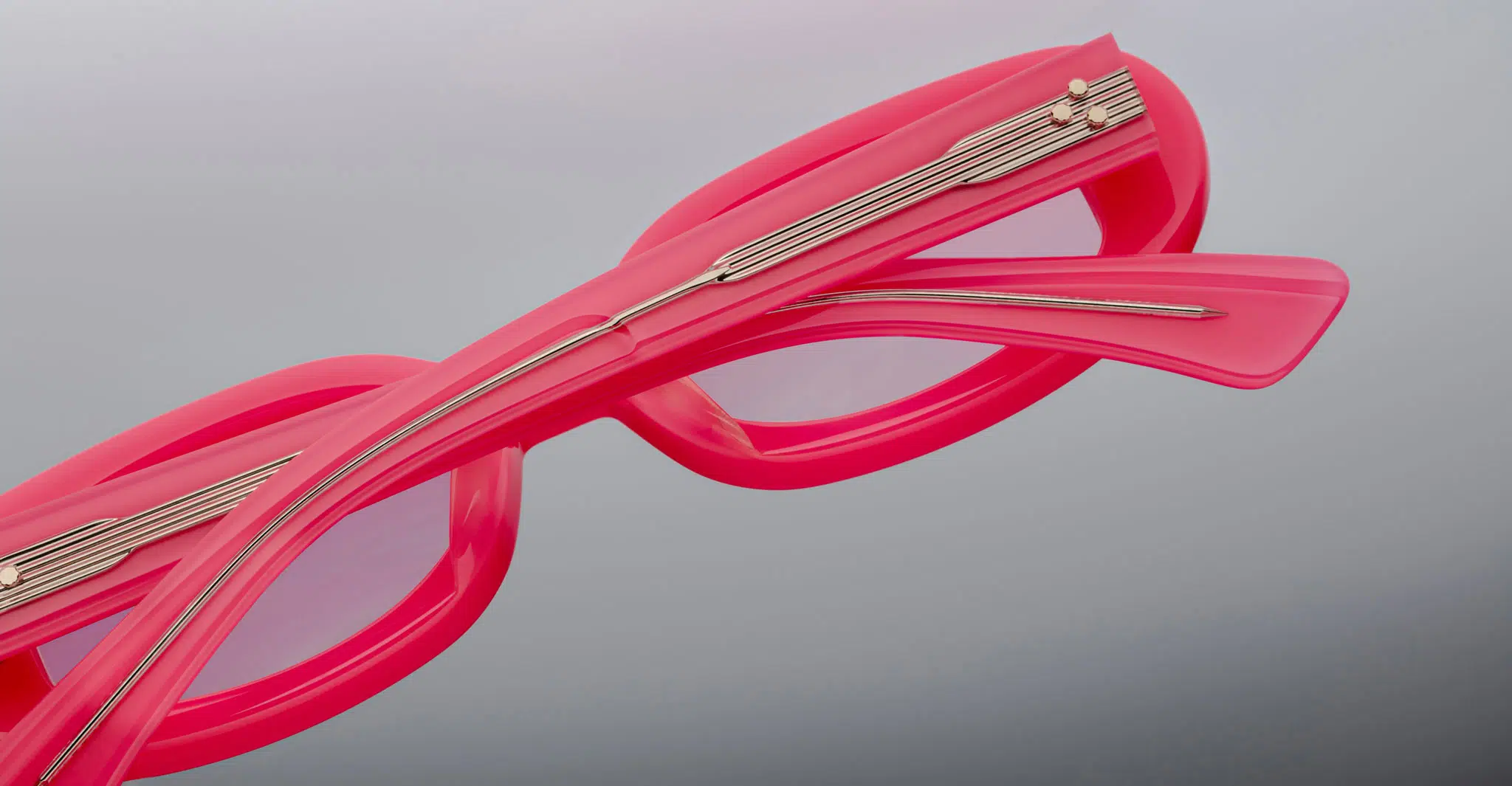 A close-up of two Jacques Marie Mage Besset eyeglasses in bright pink with metallic temple accents, stacked atop each other against a plain gray background.