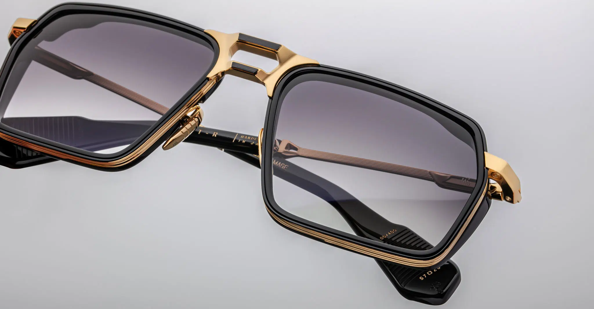 Close-up image of Jacques Marie Mage GT-R square sunglasses featuring gold and black frames, gradient gray lenses, and intricate metalwork on the temples, set against a plain light background.