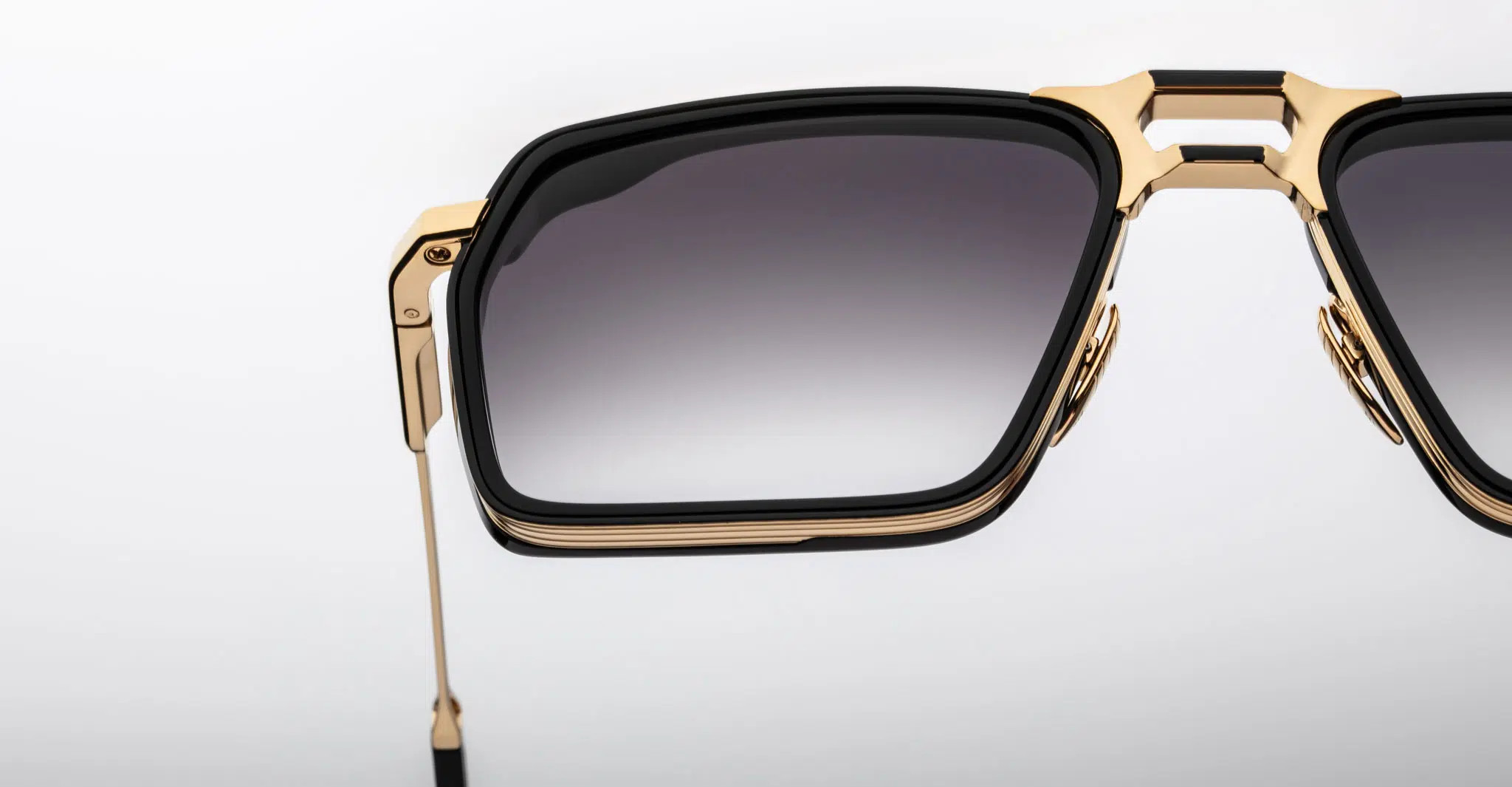 Close-up of the right half of Jacques Marie Mage GT-R sunglasses featuring a black and gold frame and gradient dark lenses, set against a plain white background.