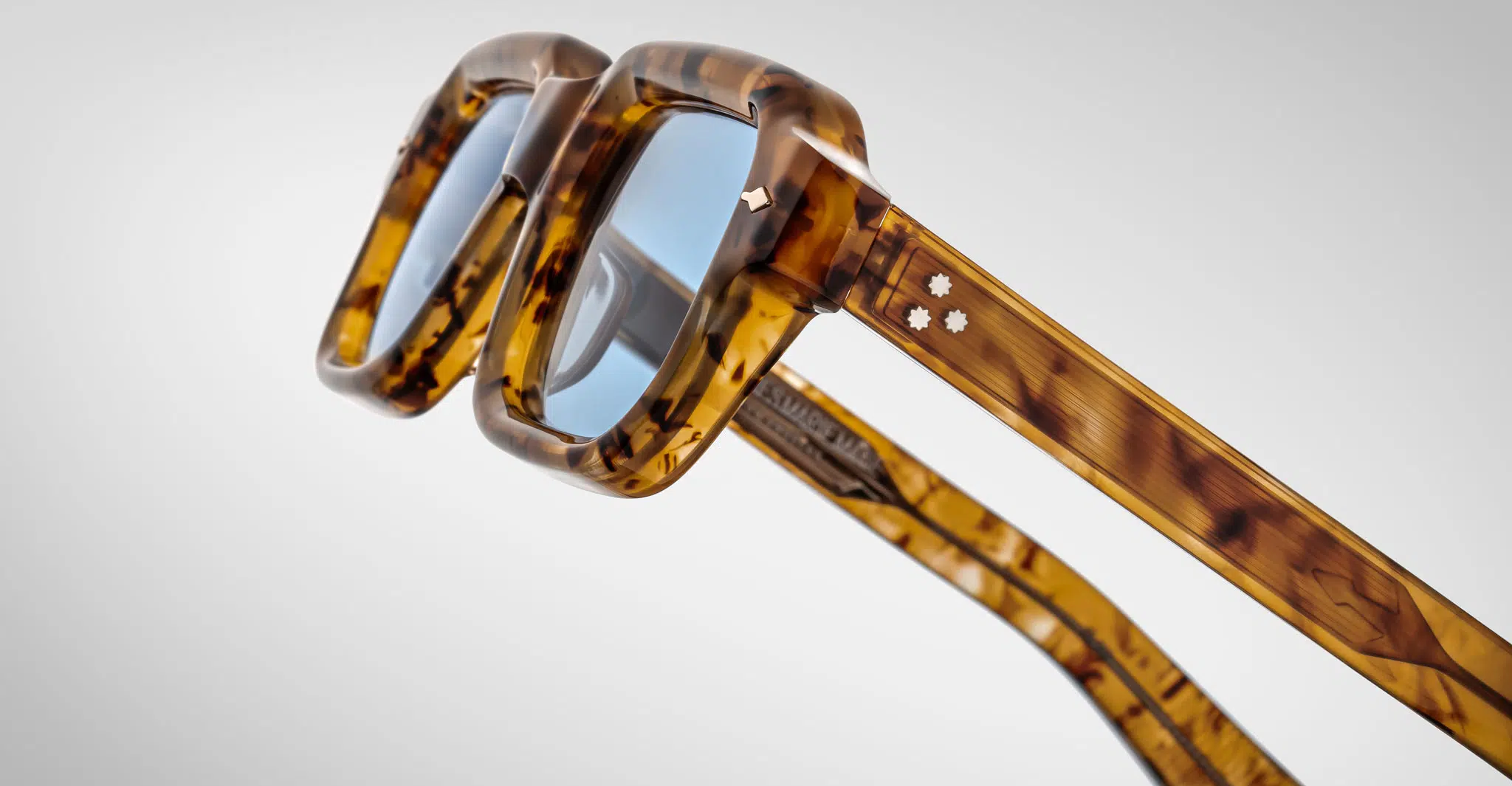 Close-up view of Jacques Marie Mage Sandro square eyeglasses in a tortoiseshell pattern, featuring blue-tinted lenses and two small star-shaped metal accents on the temples, shown against a plain background.