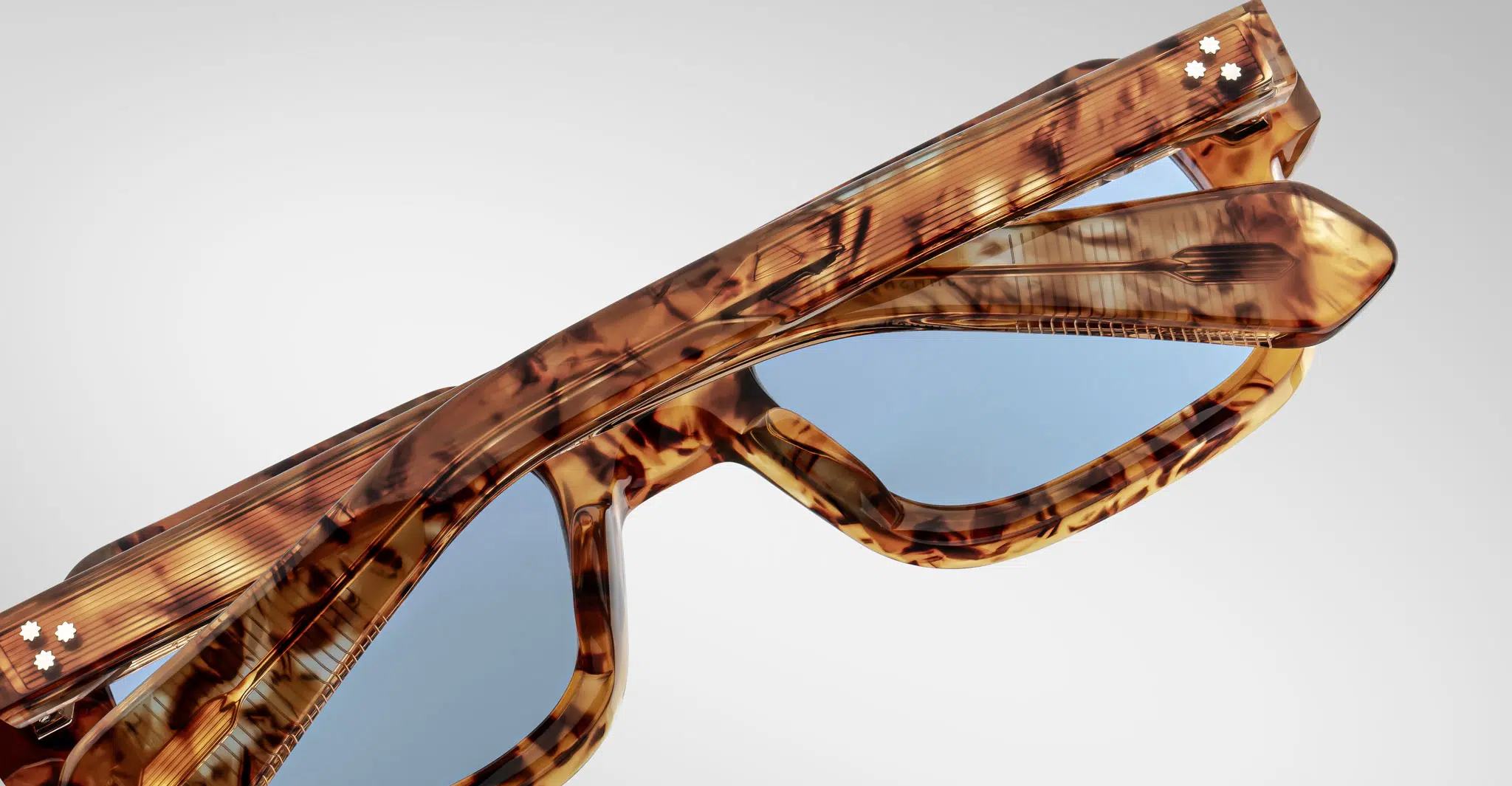 A close-up of two pairs of Jacques Marie Mage Sandro tortoiseshell sunglasses with blue-tinted lenses, stacked at an angle against a plain light background.