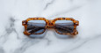 A pair of Jacques Marie Mage Sandro square tortoiseshell sunglasses with blue-tinted lenses rests on a white marble surface.