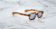 A pair of Jacques Marie Mage Sandro tortoiseshell square sunglasses with blue-tinted lenses rests on a white marble surface.