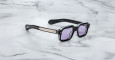 The Jacques Marie Mage Sandro sunglasses feature a black rectangular frame, light purple lenses, and metallic temple detailing, showcased on a white marble surface.