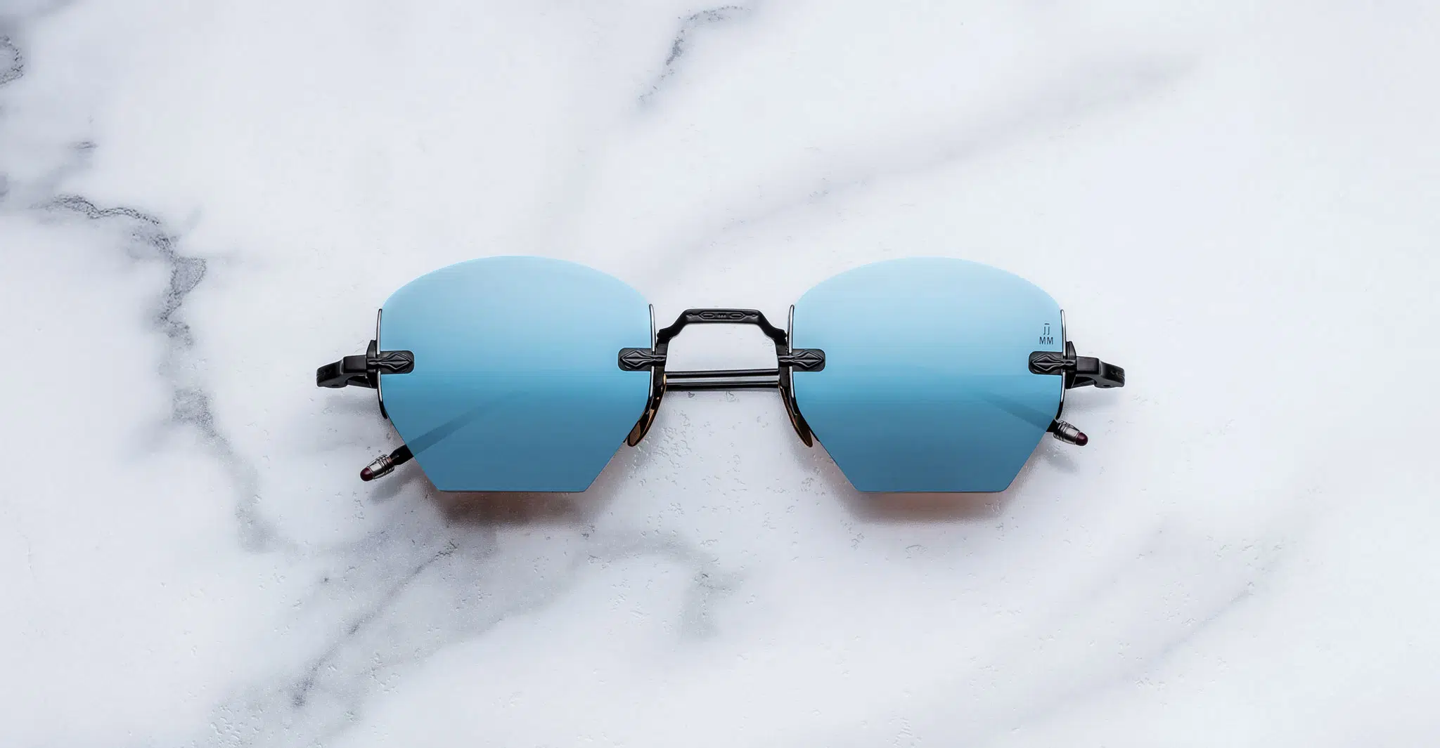 Jacques-Marie-Mage-Oatman-Lagoon-JMMOA-K8-Front-Dan-Deutsch The Jacques Marie Mage Oatman sunglasses feature frameless blue gradient lenses and black arms, showcased on a white marble surface.