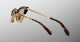 The Jacques Marie Mage Sartre sunglasses feature brown and gold frames with dark lenses, gold metal arms with a diamond pattern, and tortoiseshell ends, displayed against a light gray gradient background.