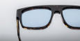 Close-up of the upper half of Jacques Marie Mage Ritz sunglasses, featuring a dark tortoiseshell frame and light blue lenses, set against a plain, light background.