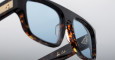 Close-up of Jacques Marie Mage Ritz tortoiseshell eyeglasses with blue-tinted lenses, gold detailing on the arms, and a signature reading by Cut on the inner side of one arm.