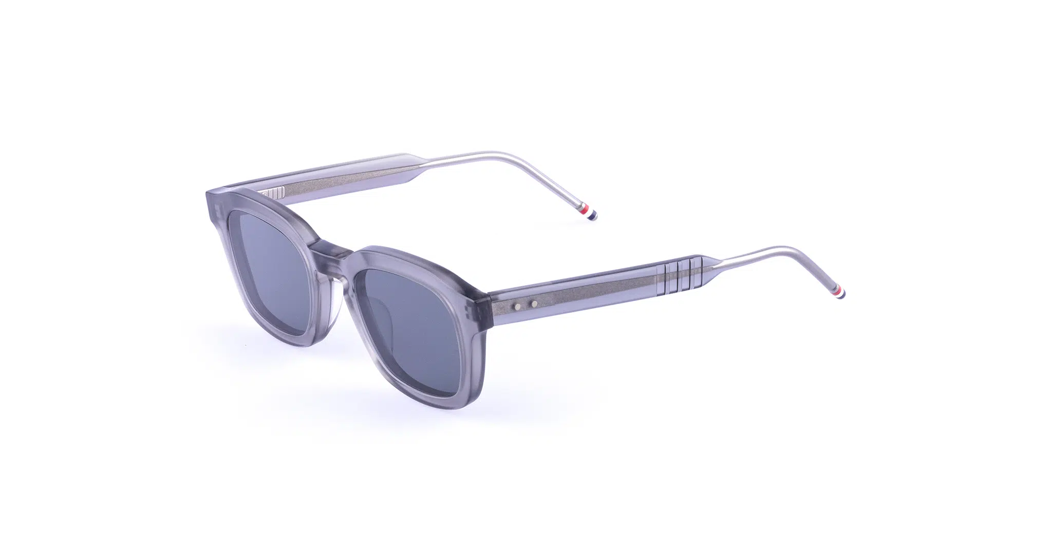 A pair of gray, rectangular Thom Browne 412 Sunglasses with thick transparent frames and dark lenses. The arms are silver with thin colored stripes near the tips, set against a plain white background.