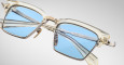 Close-up of Jacques Marie Mage Alin: stylish, translucent square eyeglasses with light blue lenses and gold accents, set against a plain background. The modern frames have a sleek, refined look and high-quality finish.