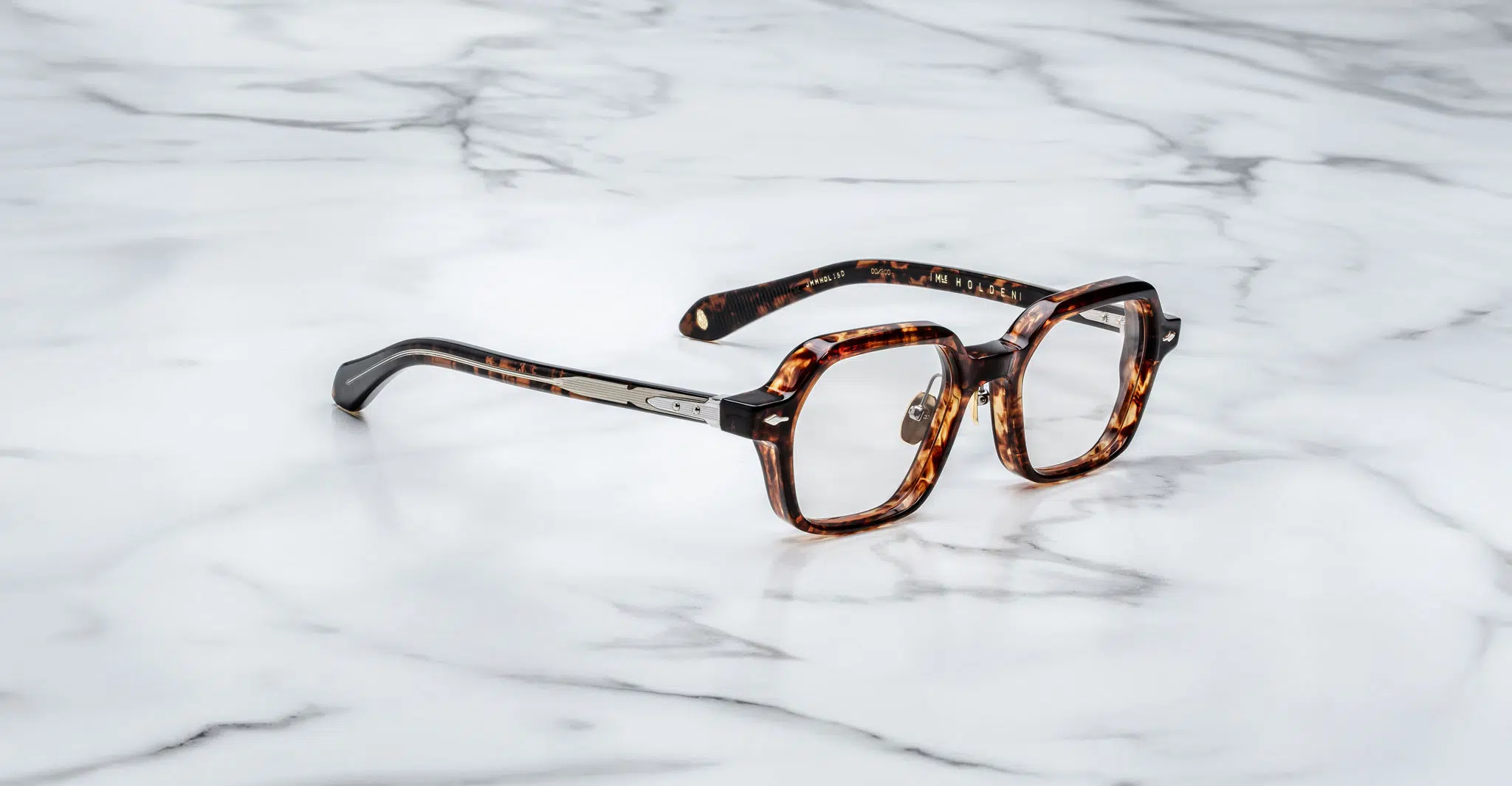 Jacques-Marie-Mage-Holden-Samoa-JMMHOLRX-15D-3-4-Dan-Deutsch Jacques Marie Mage Holden eyeglasses featuring tortoiseshell-patterned, geometric, slightly oversized frames with metallic hinges, displayed on a white marble surface.