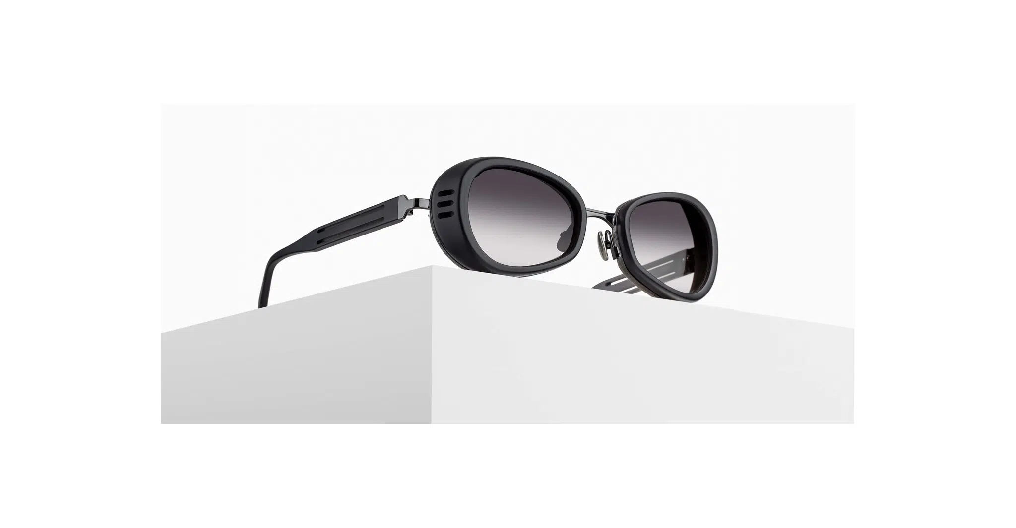 3/4 view of Matsuda 10616H sunglass in matte black with grey gradient lenses on a pedestal