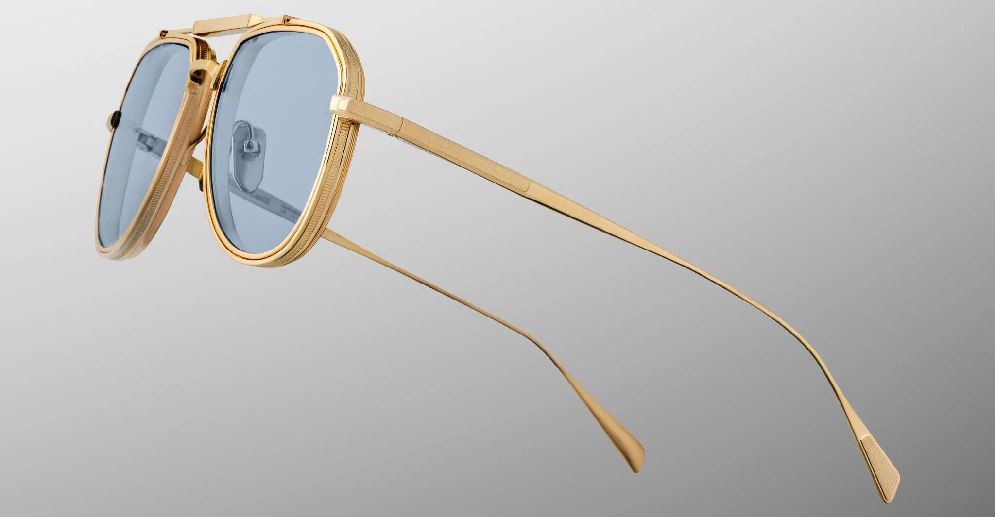 The Jacques Marie Mage Commander sunglasses, featuring gold frames, blue-tinted lenses, thin arms, and a double bridge design, are displayed in close-up against a light gray background.