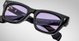 Close-up of Jacques Marie Mage Dealan black rectangular eyeglass frames with purple-tinted lenses. The inside temple arm shows the brand and manufacturing details against a plain, light background.